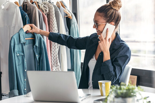 Fashion designer holding shirt and talking on mobile phone in office