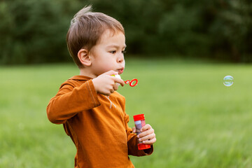 childhood, leisure and people concept - little boy blowing soap bubbles and playing at park