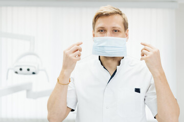 Fototapeta na wymiar Portrait of a young male medical doctor putting sterile mask in the dentist office