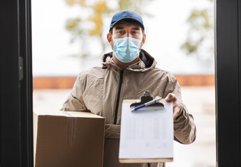 Fototapeta na wymiar health protection, mail service and pandemic concept - delivery man in face protective mask holding parcel box with clipboard at open door