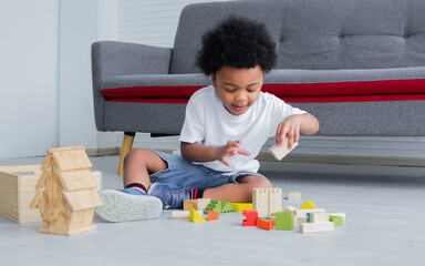 Little african cute boy playing toys, laughing and sitting on the floor in living room at home. Education and Lifestyle Concept.