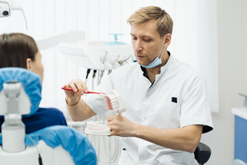 Dentist showing the correct dental hygiene using mock-up of skeleton of teeth. Stomatologist doctor explaining proper dental hygiene to patient holding sample of human jaw with toothbrush.