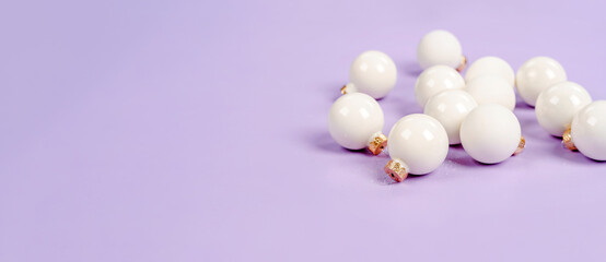 White Christmas balls lie on a purple background, a beautiful minimalistic background for Christmas and New Year