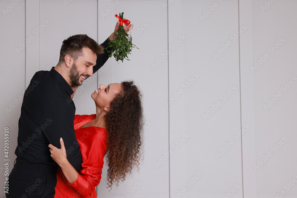 Sticker Lovely couple dancing under mistletoe bunch near light grey wall. Space for text