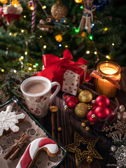 Cup of hot coffee, cocoa near a beautifully wrapped Christmas present and sweet desserts with defocused lights in the background. Relaxing and Christmas concept.