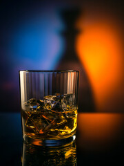 Whiskey, cognac, bourbon in a glass with ice on a mirrored table, colorful background.