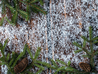Christmas frame with fir branches and cones on a wooden background covered with snow.