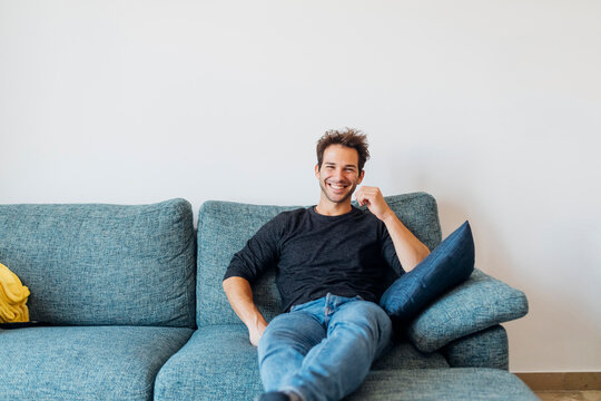 Happy young man sitting on sofa in living room at home