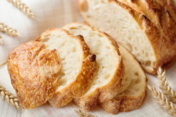 Close up of sliced traditional round wheat bread on linen towel with ears of wheat around, selective focus.