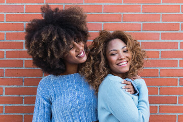 Smiling african american friends with long afro hair, glamour makeup and blue jumper in brick wall....