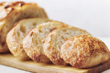 Close up of slices of freshly homemade wheat bread on wooden board against light background, selective focus.