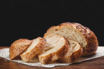Sliced freshly baked wheat bread on white napkin on wooden table on black background, selective focus.