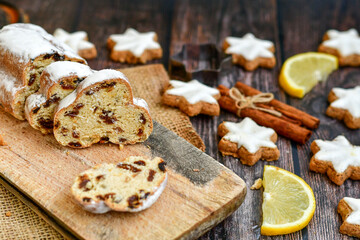 Traditional German bread   Christmass stollen  cake ,gingerbread star shaped   cookies and cinnamon sticks    on   wooden background with lights . Christmas  card background  . Holiday wallpaper