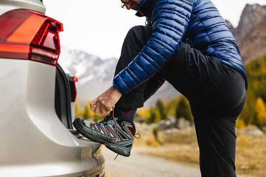 Senior man tying lace of hiking boot at car trunk on vacation