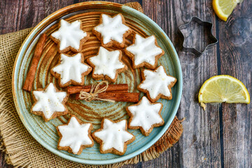 Traditional German bread   Christmass stollen  cake ,gingerbread star shaped   cookies and cinnamon sticks    on   wooden background with lights . Christmas  card background  . Holiday wallpaper