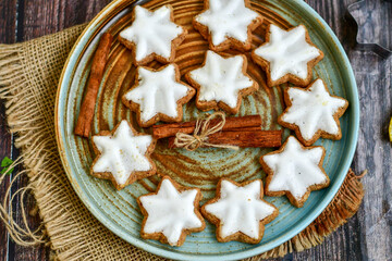 Traditional German bread   Christmass stollen  cake ,gingerbread star shaped   cookies and cinnamon sticks    on   wooden background with lights . Christmas  card background  . Holiday wallpaper