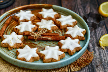 Traditional German bread   Christmass stollen  cake ,gingerbread star shaped   cookies and cinnamon sticks    on   wooden background with lights . Christmas  card background  . Holiday wallpaper