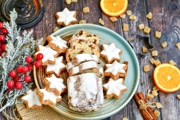 Traditional German bread   Christmass stollen  cake ,gingerbread star shaped   cookies and cinnamon sticks    on   wooden background with lights . Christmas  card background  . Holiday wallpaper