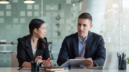 Two business people discuss investment project working and planning strategy. Businessman and businesswoman talking together with tablet at office.