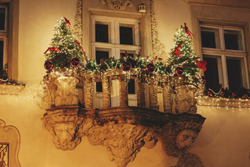 Stylish christmas trees, branches, red ornaments in lights illumination on balcony of building in evening. Atmospheric magic time. Christmas festive decor for winter holidays. Merry Christmas!