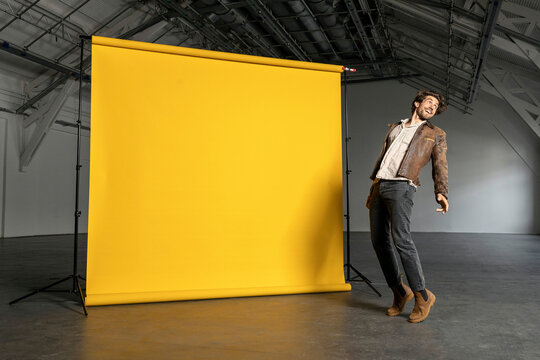Smiling businessman on tiptoe by yellow backdrop