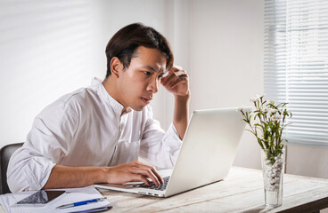 Male overwork. Upset Asian young man in white shirt working alone at home office, exhausted, late home cause financial problem and hard work. Overthinking Unhappy angry and trouble in office concept