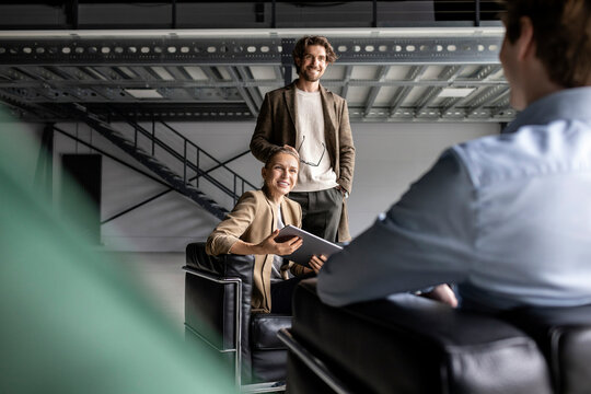 Smiling businessman and businesswoman discussing with colleague in industrial hall - Powered by Adobe
