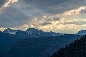 Golden hour and sunset with sunbeams through the clouds, as viewed while driving on the Going to the Sun Road in Glacier National Park in Montana on a beautiful sunny summer evening