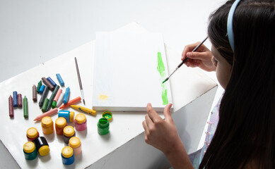 beautiful girl, holding brush, painting a canvas with green paint, next to colored paints, photo seen from above.