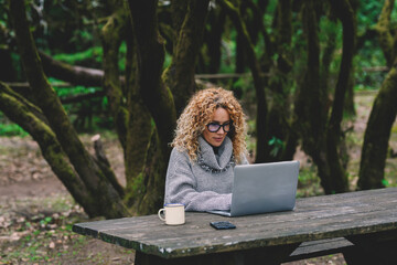 Young adult modern woman use computer laptop sitting at the table in the forest park. People with...