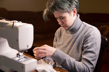 The girl sews while sitting at the sewing machine. Skill, hobby, profession.