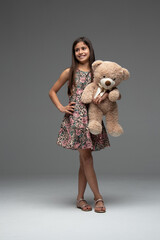 beautiful girl in flowered dress looking to the side with her hand on her waist and the other hand holding her teddy bear.