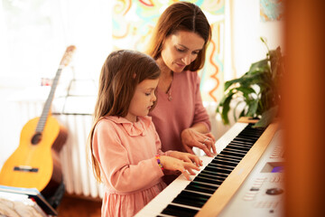 Woman and girl playing a piano. Beautiful mom teaching her daughter playing a piano.