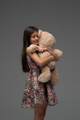 beautiful girl in a flowery dress hugging her teddy bear with her eyes closed.