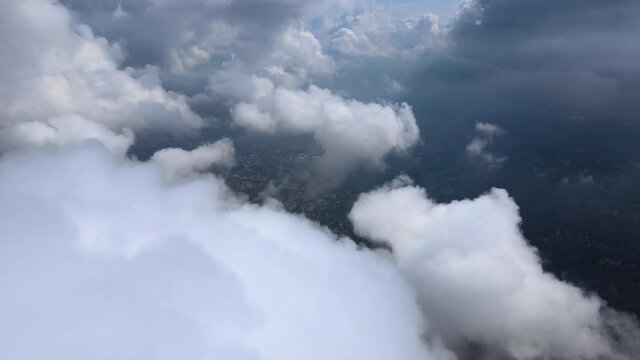Aerial view from airplane window at high altitude of distant city covered with puffy cumulus clouds forming before rainstorm.