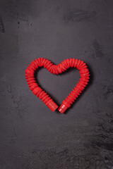 One antistress pop tube toy bent in shape of heart on black stone background