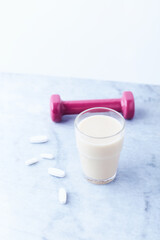 Banana coconut smoothie and sports supplements on bright stone background. Soft focus. Copy space.
