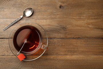 Tea bag in glass cup of hot water on wooden table, flat lay. Space for text