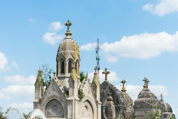  5G and 4G tower behind an old cemetery mausoleum with a background of blue sky and clouds.