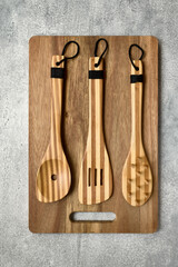 Wooden bamboo kitchen utensils lie on acacia cutting board, gray concrete background, top view