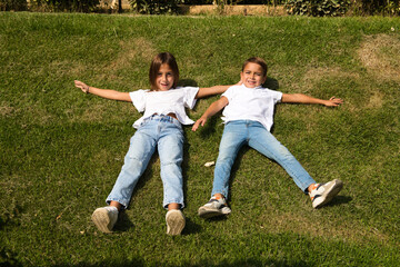 Portrait of two little brother and sister children lying on the grass. They are dressed in white T-shirts and jeans. The older sister is a transsexual girl. Concept of a united and happy family.
