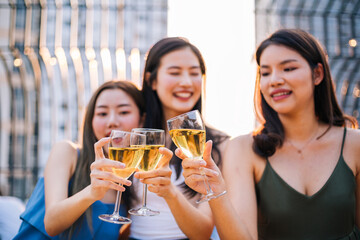 Group of happy smiling Asian girl friends celebrating party with champagne toasting drinks at rooftop cafe together, female gang chatting, laughing, night lifestyle of young people, focus on glasses