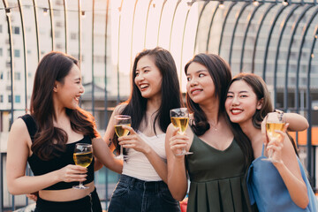 Group of happy Asian girl friends celebrating party with wine toasting drinks in sunset together, female gang chatting, laughing on smile face, night lifestyle of young people