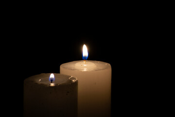 Two thick candles with light burning in the darkness.