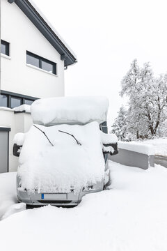 Eingeschneiter Camper mit Schnee auf dem Dach vor einem Wohnhaus