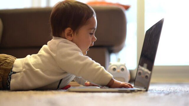 Baby lying on the floor having fun playing on his father's work computer