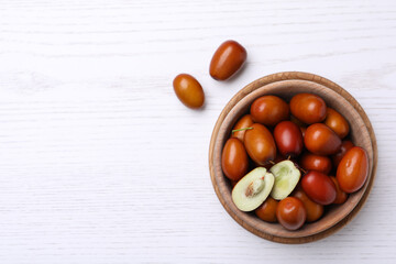 Fresh Ziziphus jujuba fruits with bowl on white wooden table, flat lay. Space for text