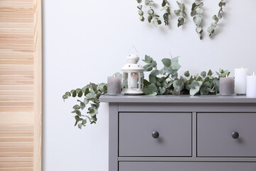 Stylish chest of drawers decorated with beautiful eucalyptus garland and candles indoors © New Africa
