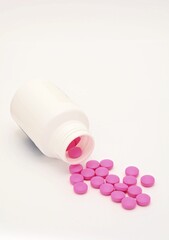 Pink pills spilled out of a white plastic bottle and scattered on white background.