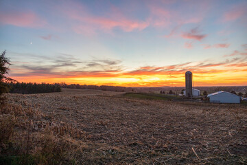 Sunset over a farm with a silo and a field